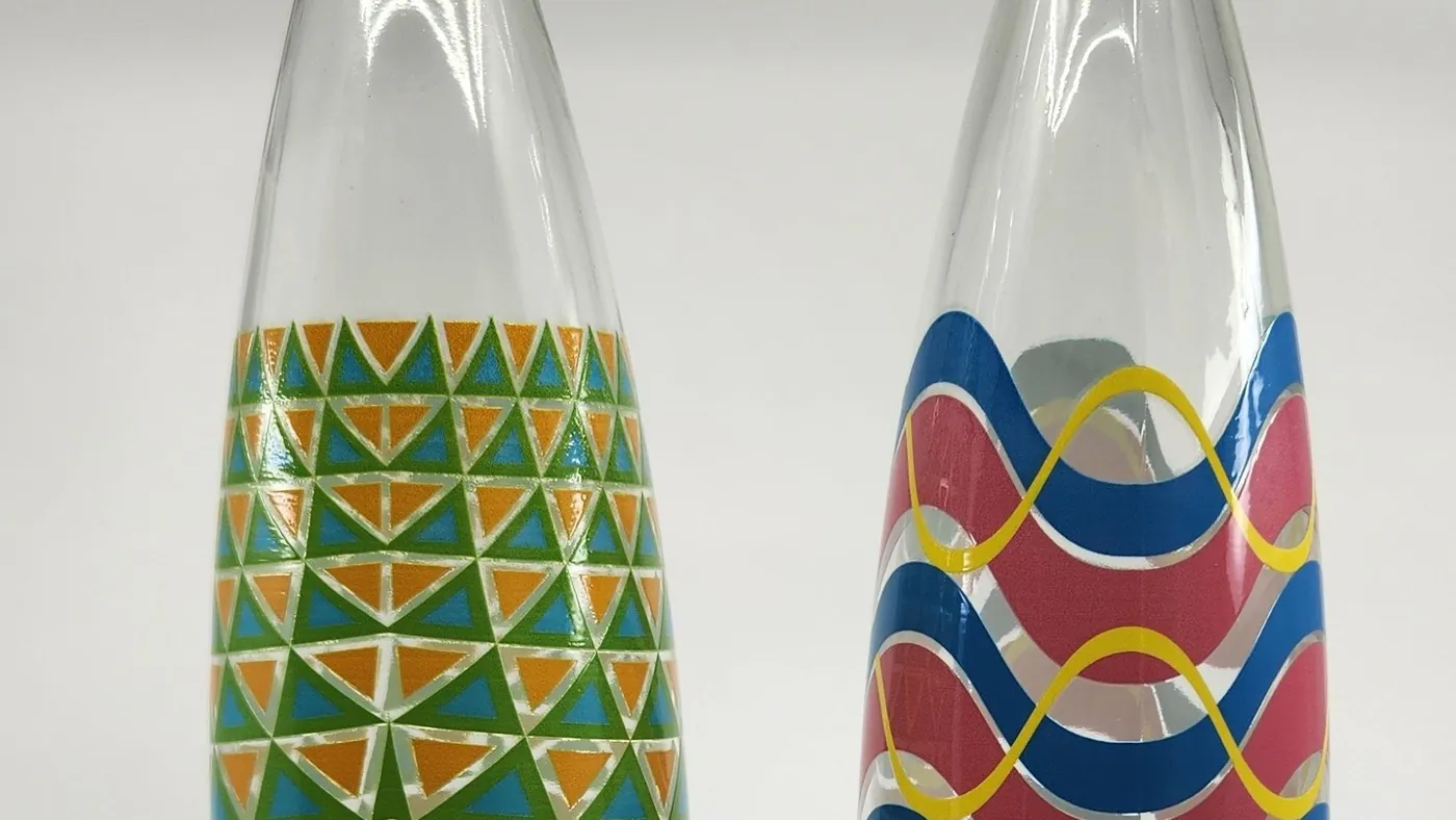 Two clear glass bottles printed all the way around with colourful geometric patterns